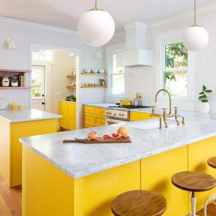 Bright yellow kitchen cabinets with marble countertops and vintage style hardware