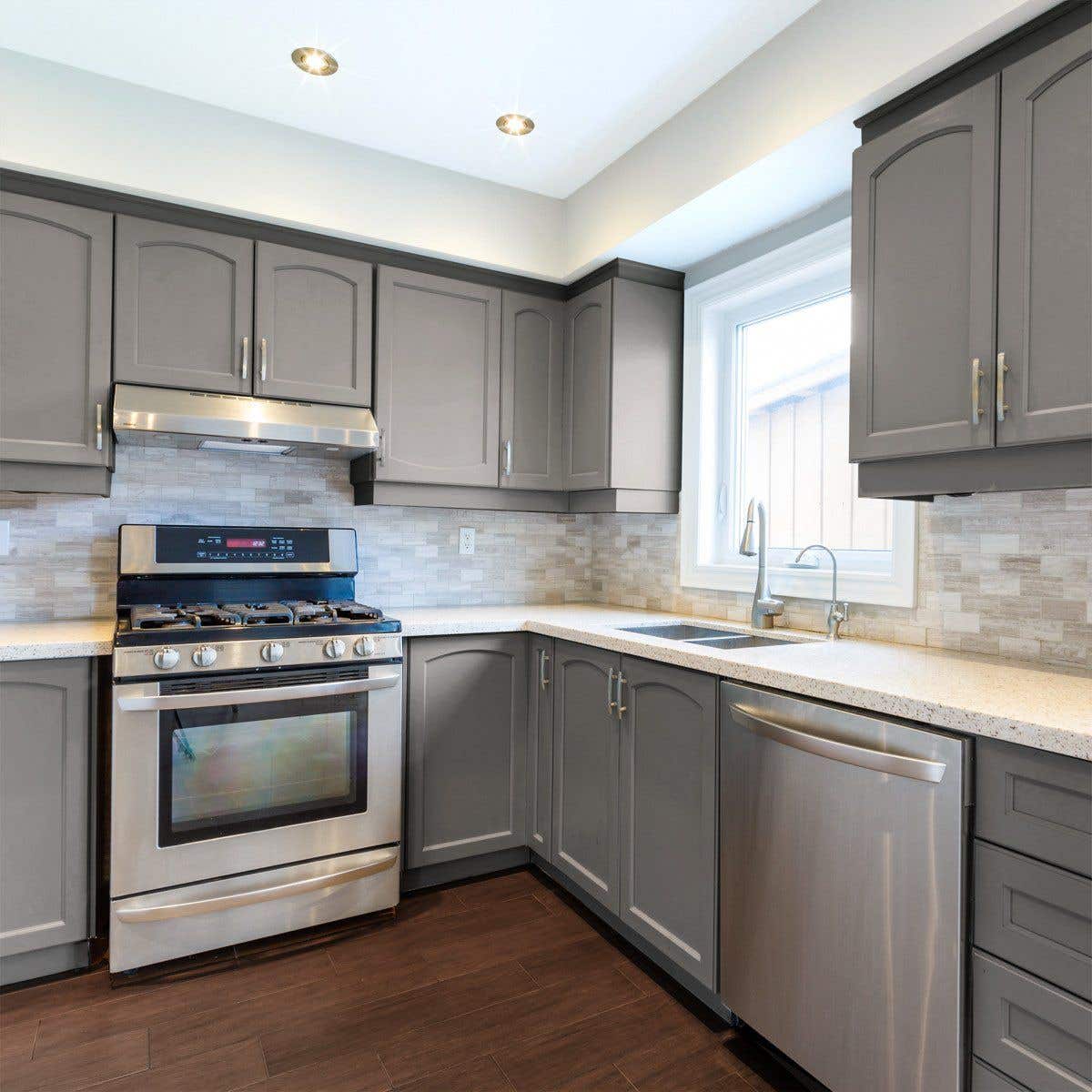 Arch panel kitchen cabinet doors with silver pulls, Brick style backsplash and Stainless Steel Appliances 