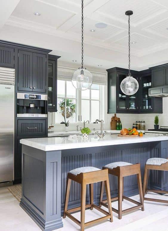 Beadboard doors kitchen cabinets paired with white countertops, Stylish Pendent Lights, and Stainless Steel Appliances 