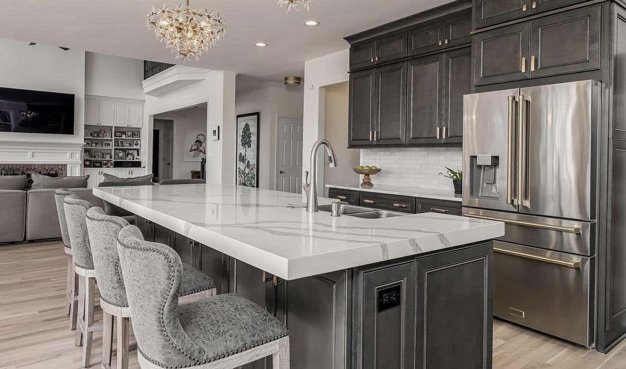 open kitchen design with gray cabinets, large island, white countertop with undermount sink, stainless steel appliances, sandler lights