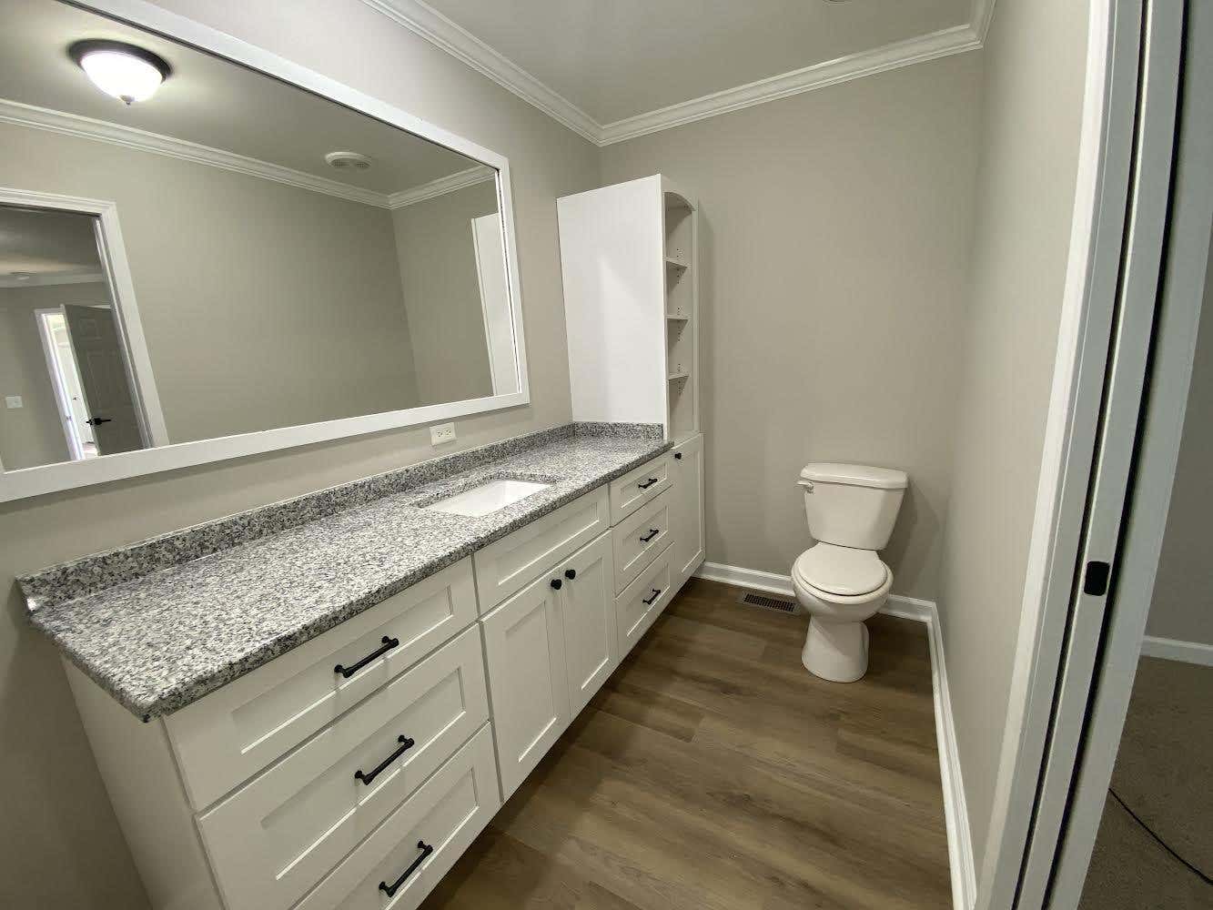 White Freestanding Bathroom Vanities with black pulls, marble countertop, one large mirror and White WaterSense Elongated Toilet