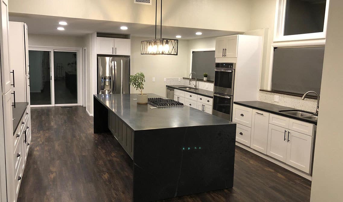 Rustic kitchen with white cabinets and black island, black waterfall countertop, pendent light and stainless steel appliances