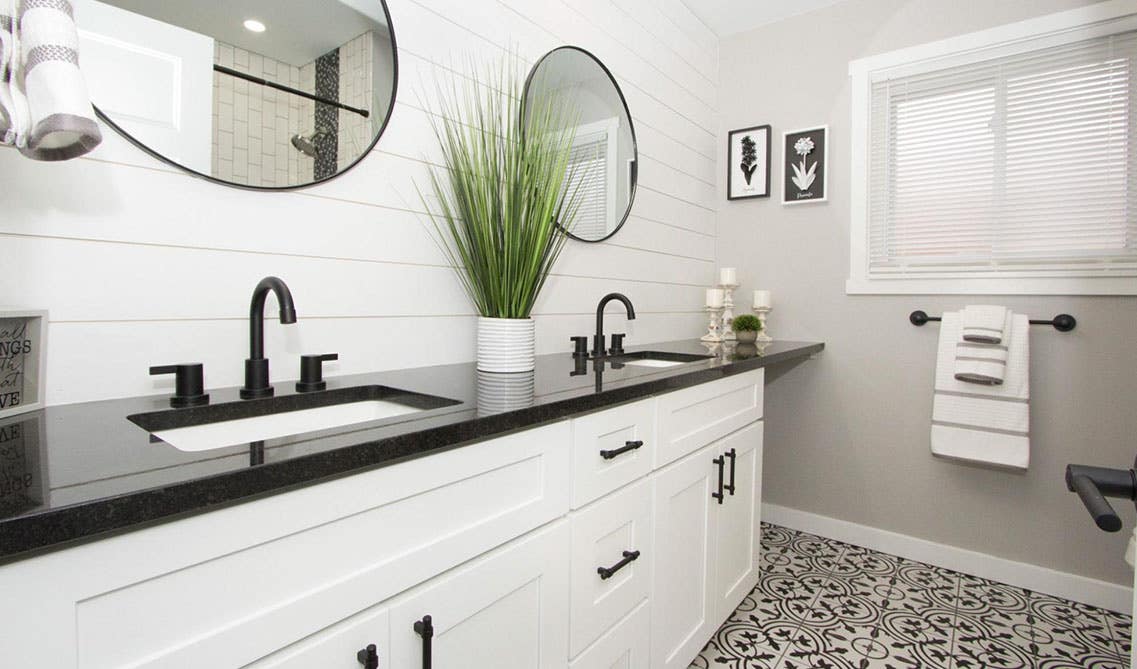 Modern Bathroom design features white vanity with black countertop, circular mirrors on shiplap wall and pattern floor tiles