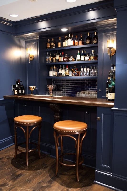 sophisticated basement bar design paired with navy blue cabinets & blue wall color and wood shelves and chairs 