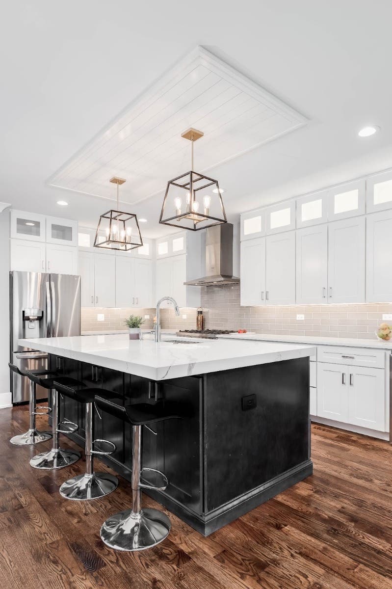 White cabinets kitchen paired with black island. marble countertop and wooden flooring