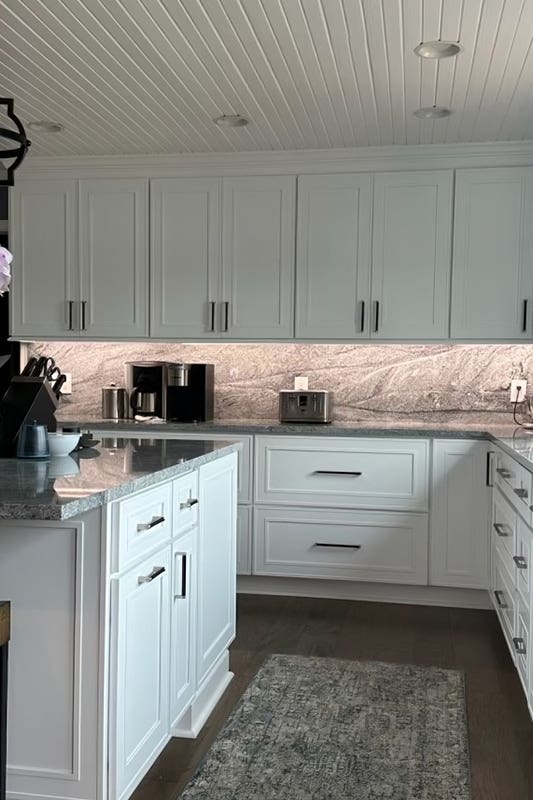 Attractive solid slab backsplashes paired with white kitchen cabinets and ceiling paneling