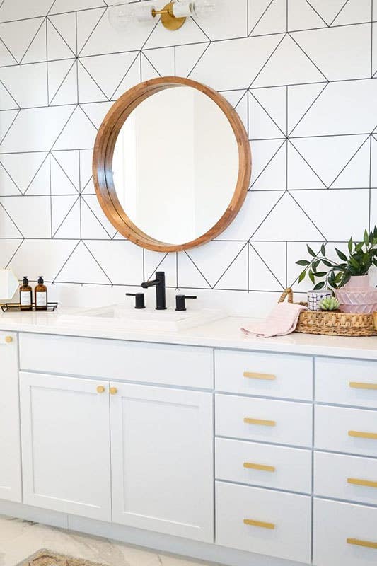 light blue modern vanity cabinets with white geometric wallpaper, circular mirror and white countertops