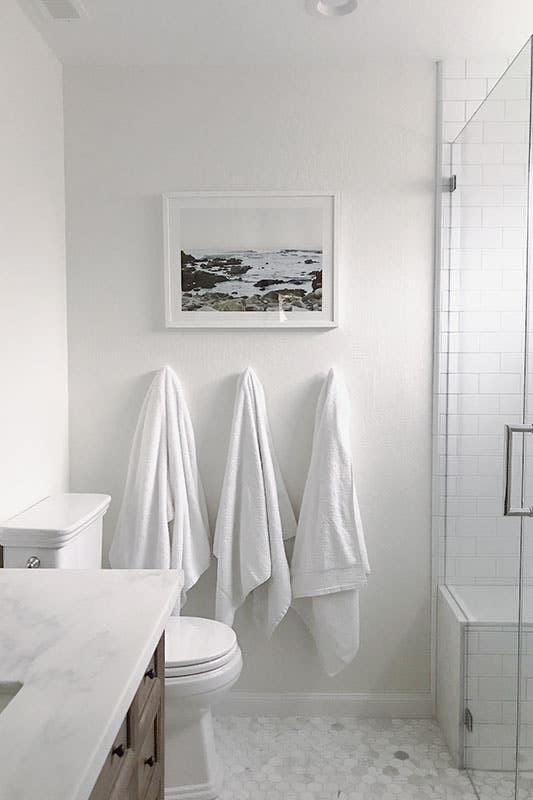white contemporary bathroom with white tile floors, white wall paint and framed beach photo on wall white wall paint and framed beach photo on wall and 3 towel on hanger