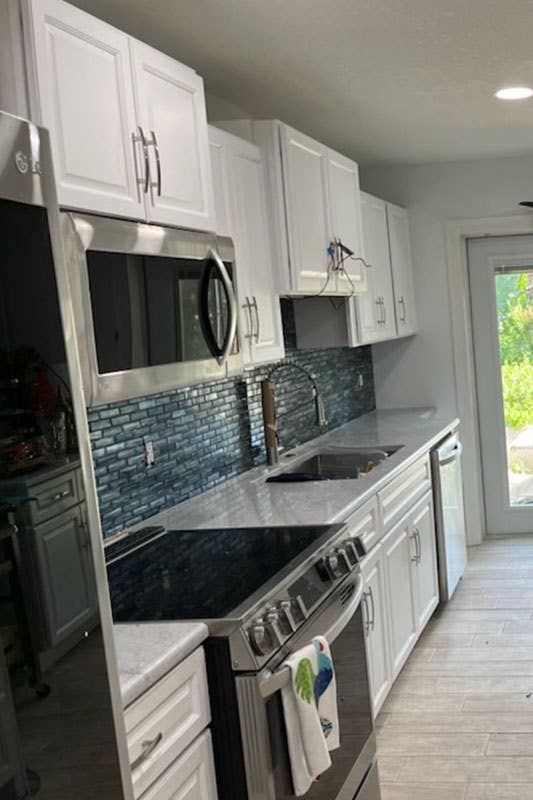 Beach inspired kitchen with white cabinets, marble countertop, spc flooring and stainless steel appliances