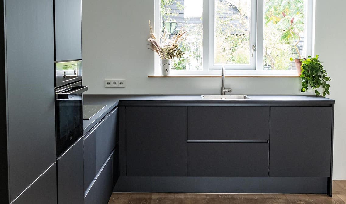 Flat panel black kitchen cabinets with black countertop, window above sink and wooden flooring