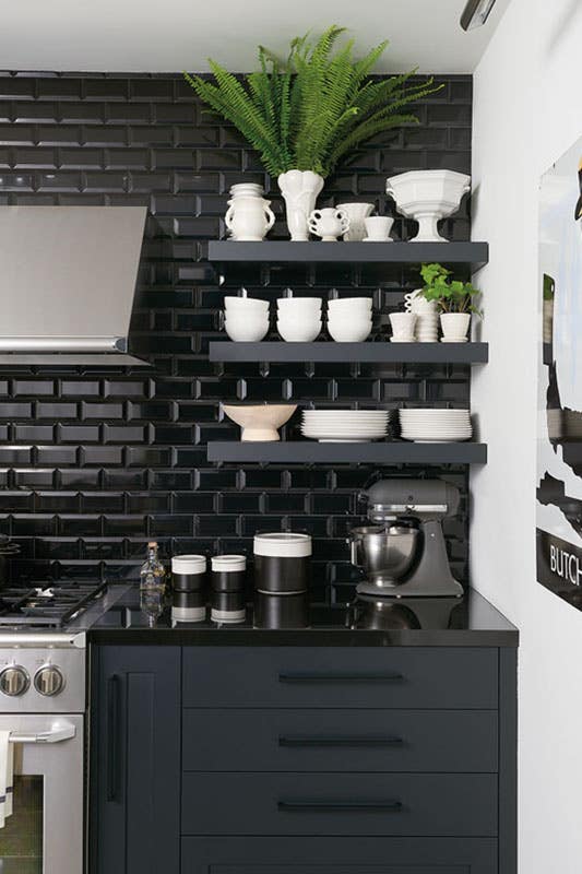 modern kitchen with black subway tile backsplash, floating shelves, black cabinets, black hardware, and stainless steel appliances