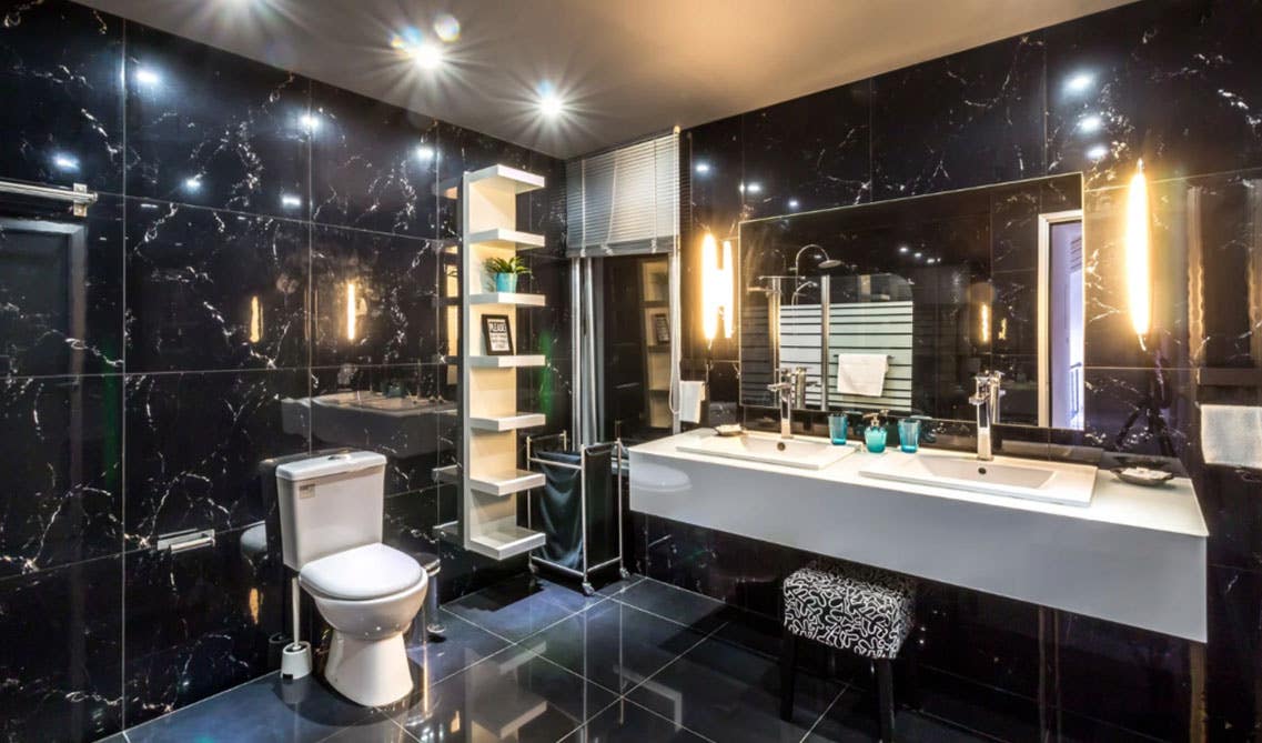 luxurious style bathroom features double sink countertops with mirror, white floating shelves and black wall and floor tiles 