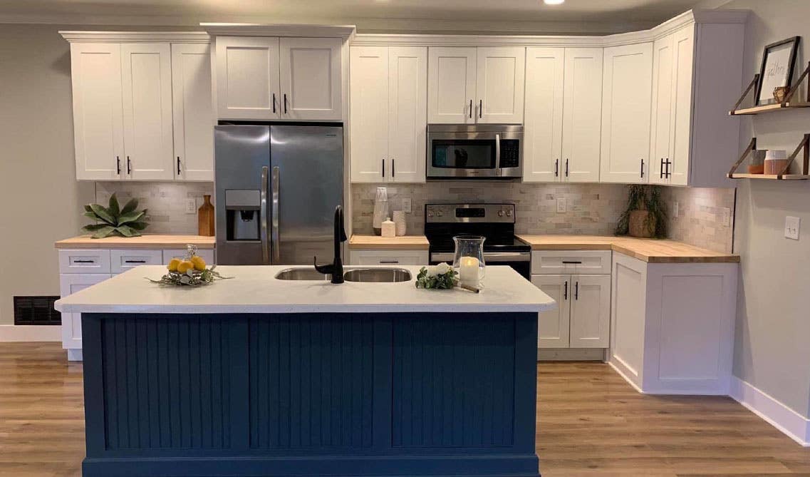 Beautiful kitchen features white cabinets on top and blue for the kitchen island, marble countertop and wooden floors. 