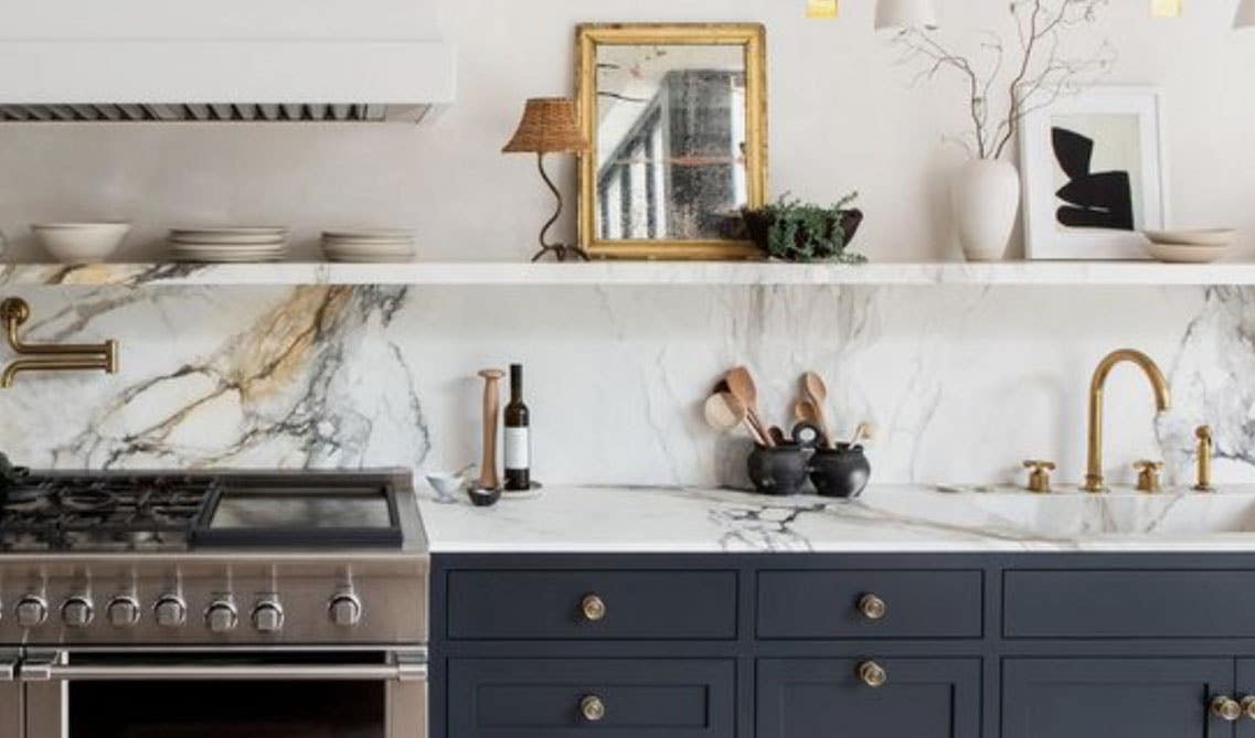 Blue kitchen cabinets with marble shelf affixed to the top of the backsplash