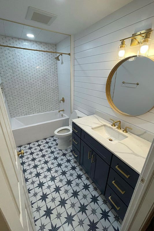 Small bathroom design with navy blue vanity, pattern floor tile and gold accent hardware 