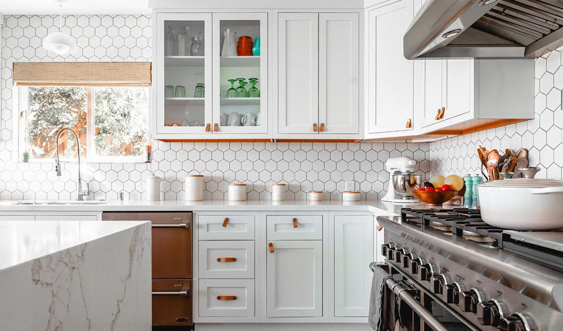 Bright White cabinets with bold wallpaper, island with waterfall countertop, stainless steel stove 