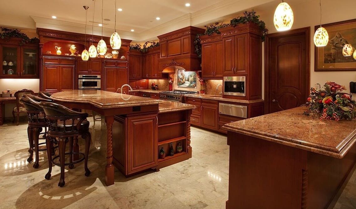 cherry cabinets paired with cream-colored wall paint, warm brown granite countertops, and creative blown glass pendant lights