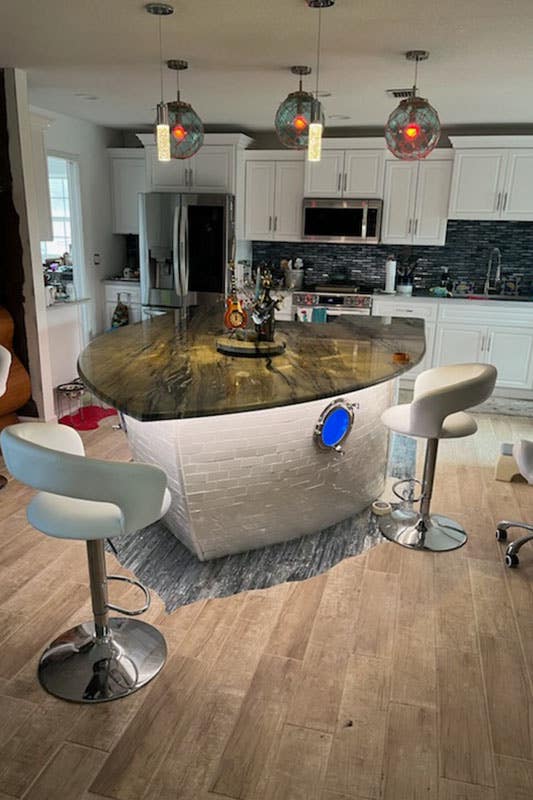 Coastal inspired kitchen features white cabinets, blue backsplash, ship shape dining area and wooden floors. 