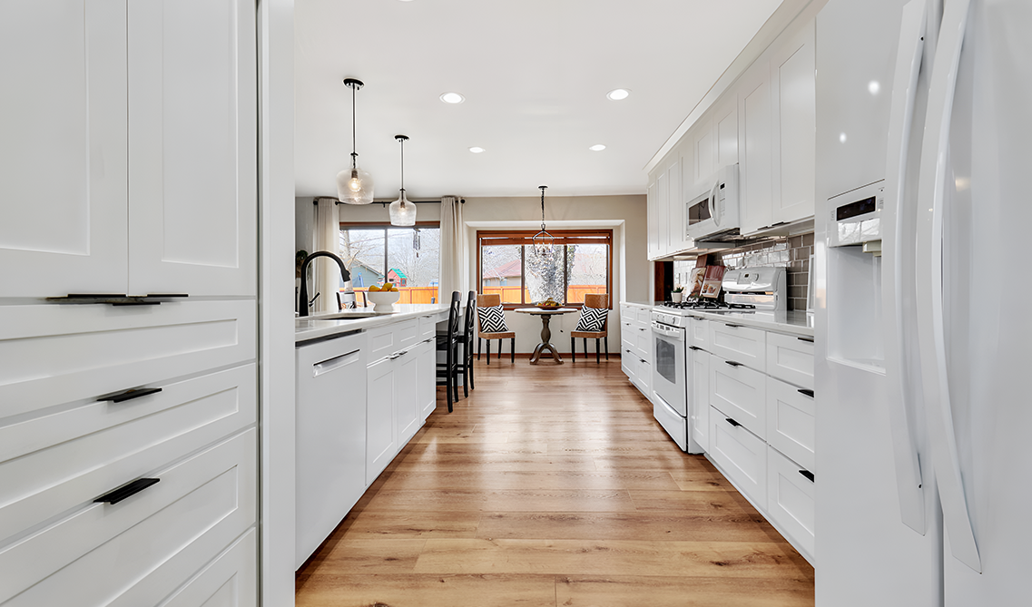 White shaker kitchen cabinets paired with white appliances, black hardware and wooden flooring 