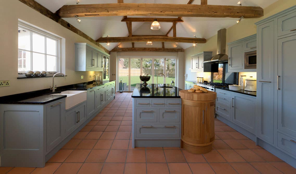 French Country inspired kitchen with pastel blue tones Cabinets, black countertop, farmhouse sink and wooden beams.