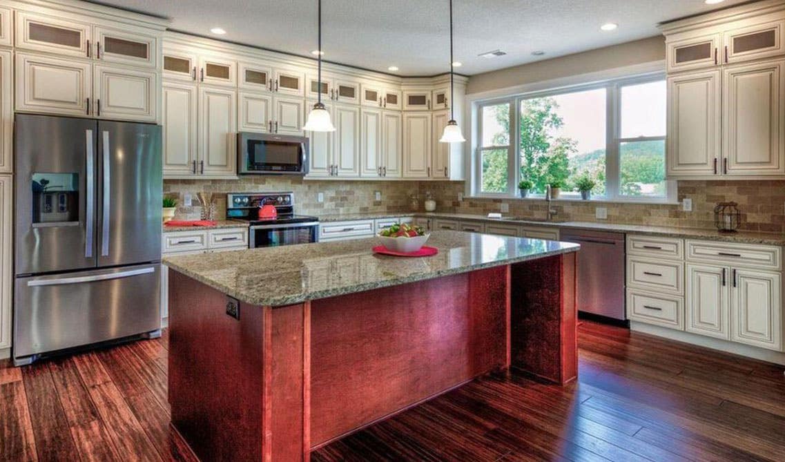 cream cabinet kitchen with dark brown color island with marble countertop, pendent lights and wooden flooring 