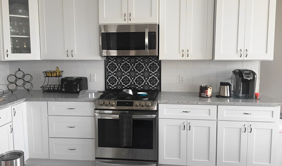White cabinets paired with stainless steel appliances, quartz countertop and pattern backsplash 