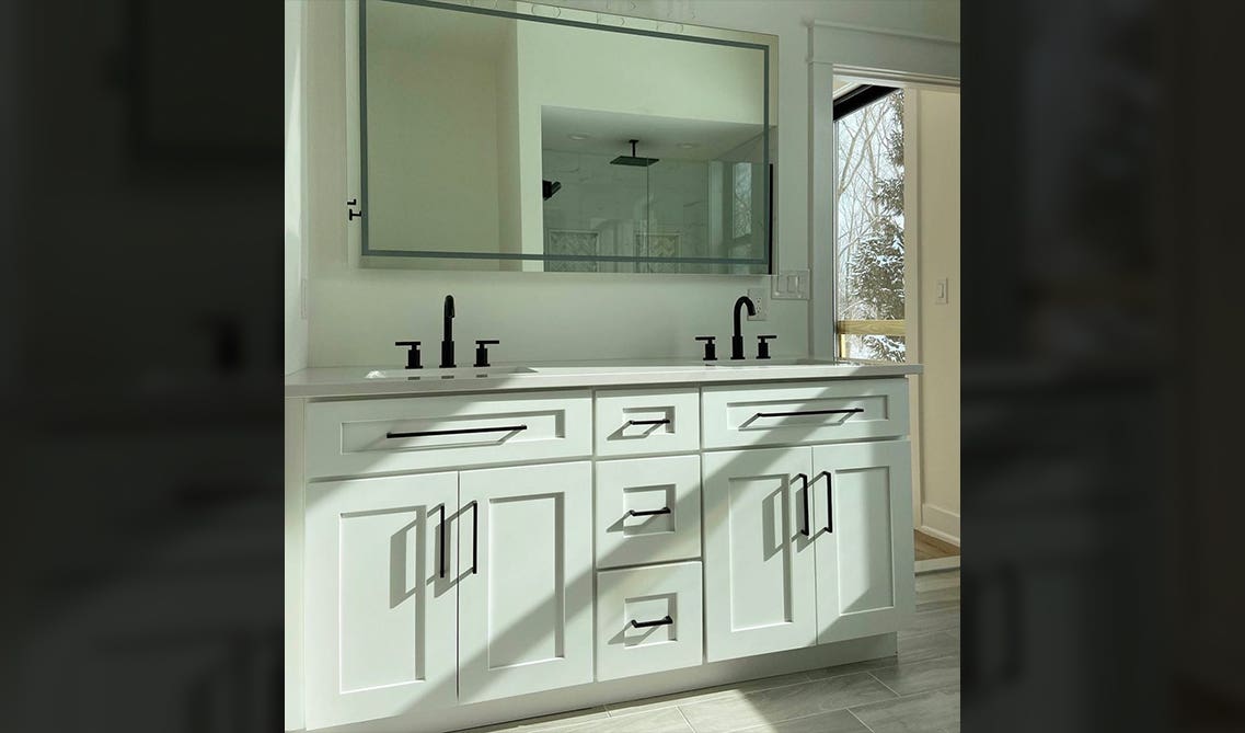 White bathroom cabinet wit black hardware and large rectangle mirror