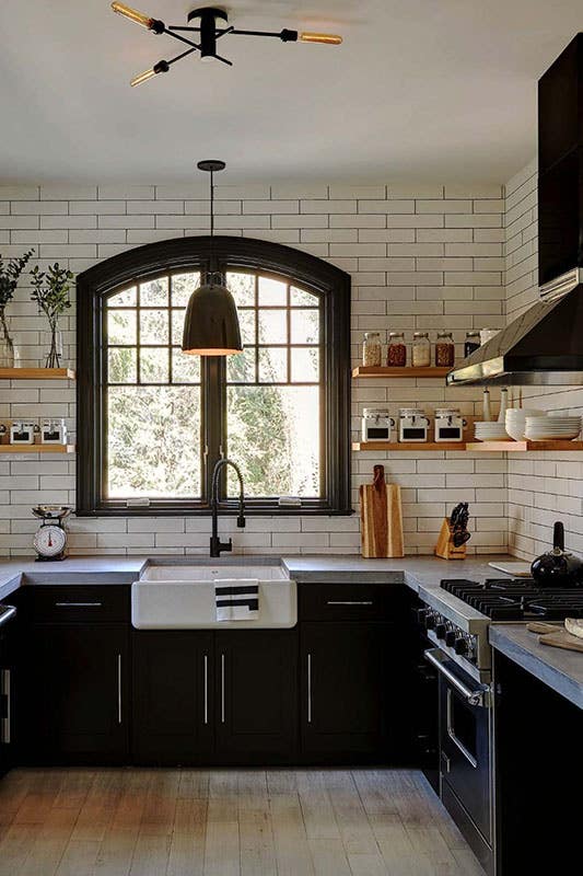 Modern industrial farmhouse kitchen with black cabinets, silver hardware, white subway tile backsplash and open shelving with cement countertops