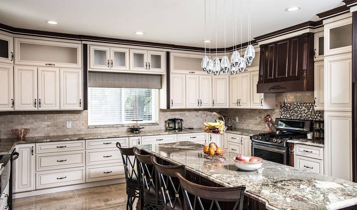 Light cabinets with dark crown molding, large island with chairs, and marble tile flooring