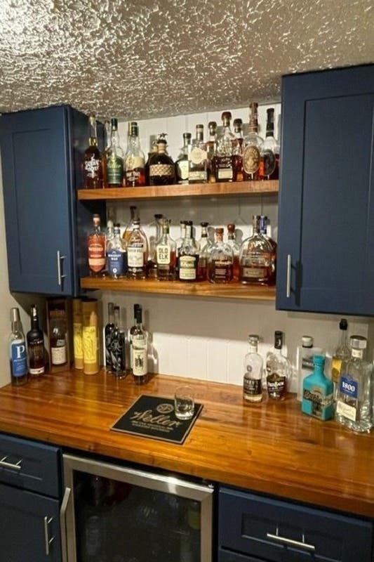 basement bar design with navy blue cabinets and open shelving displaying bottles 