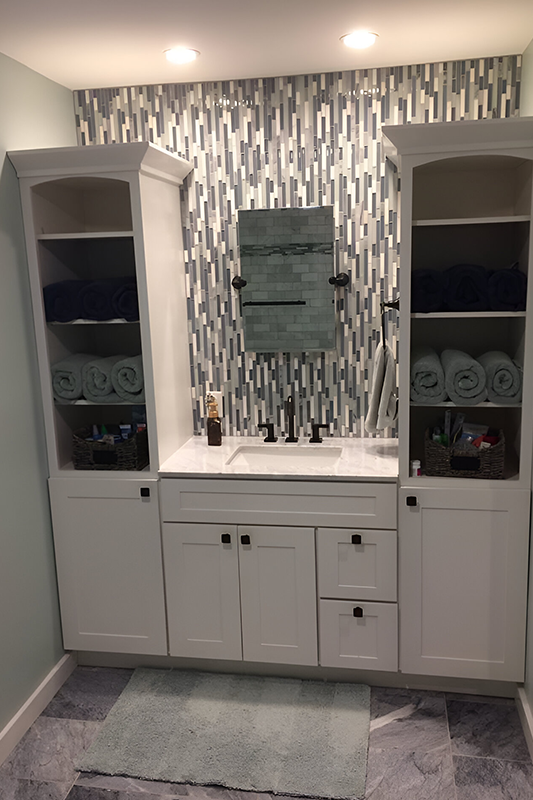 Doorless bathroom linen cabinets displaying neatly folded towels and linens,