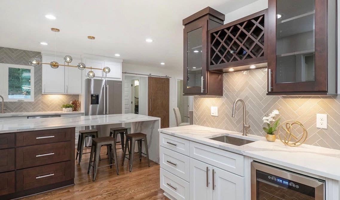 Dual tone kitchen design with white and brown cabinets, marble countertops, statement lights and large island