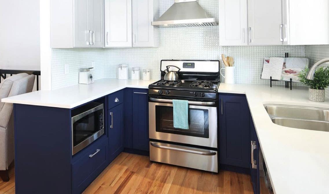 Kitchen with dual tone cabinets, white countertop, and stainless steel ducted range hood