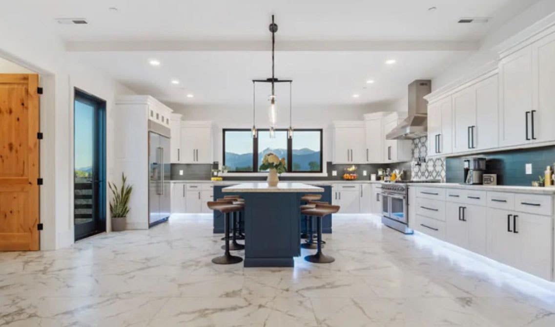 Eclectic kitchen features white cabinets, blue cabinets island, matt black hardware and marble tile floor. 