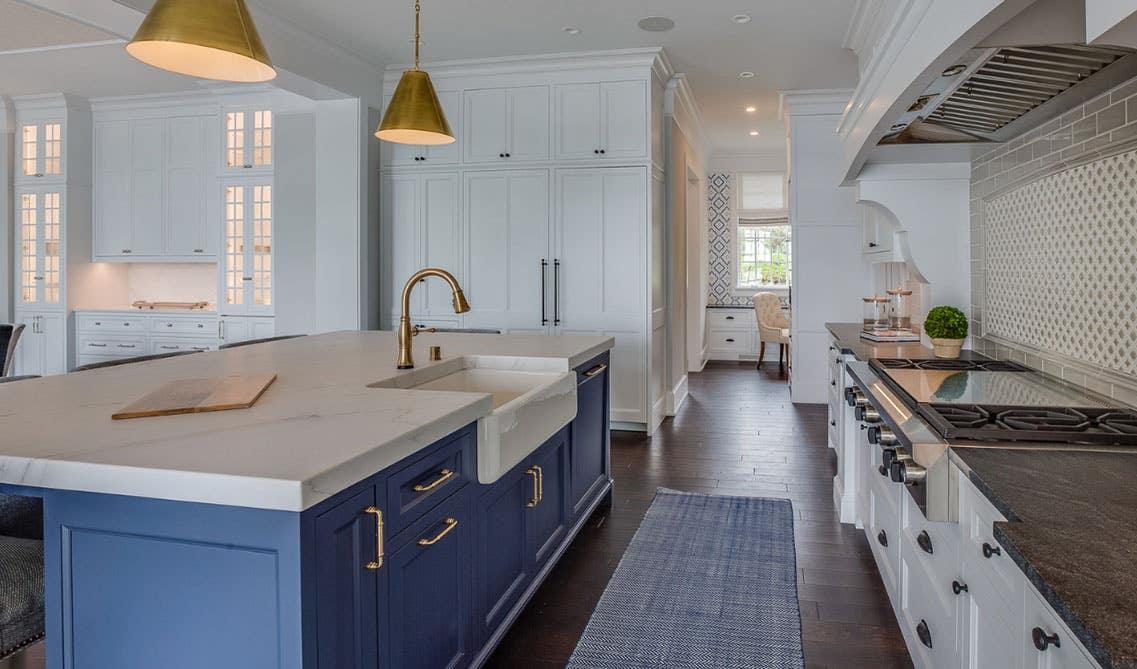 Farmhouse style kitchen features white cabinets, blue cabinet island with marble countertops and farmhouse sink