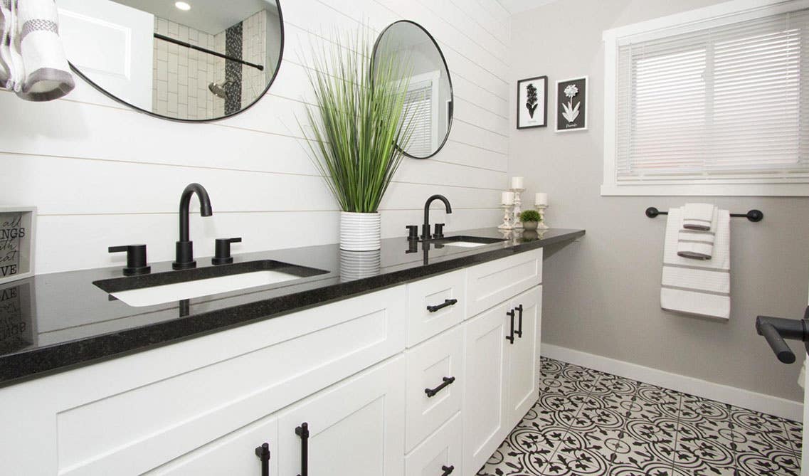 white farmhouse vanity with black countertop and shiplap wall, pattern tile, round mirrors 