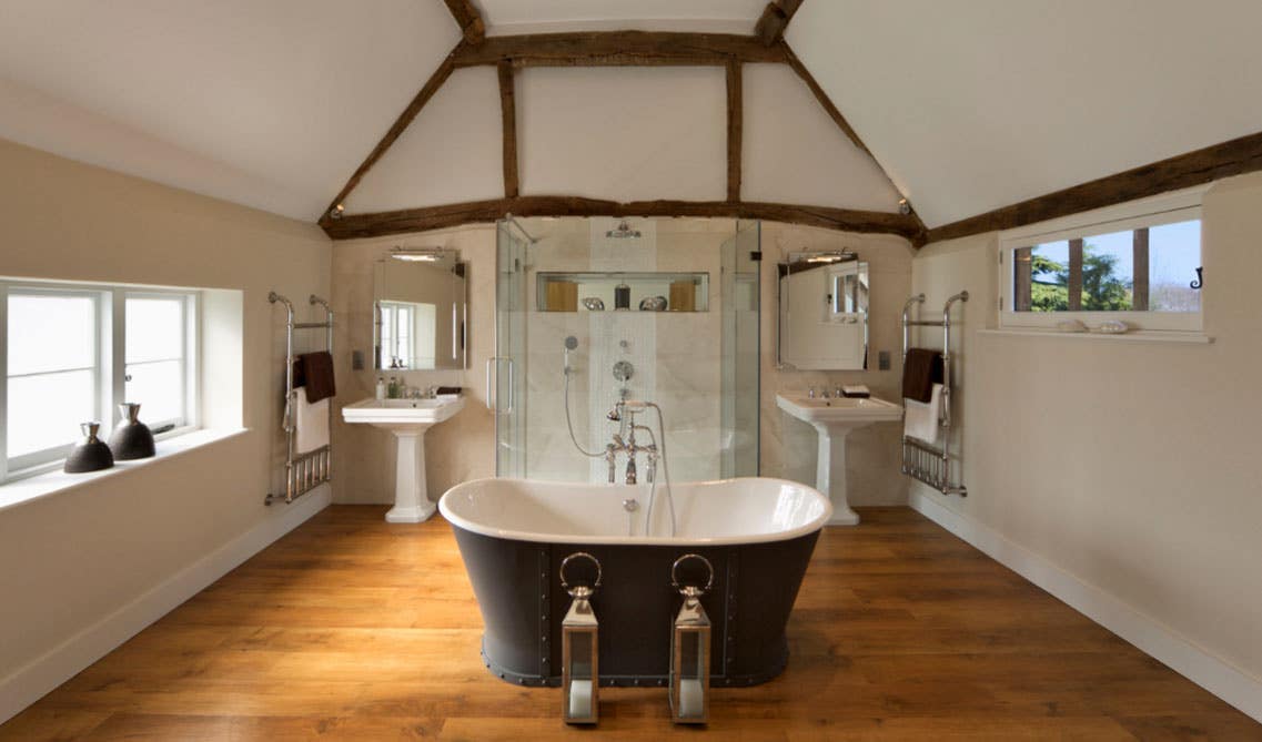 Farmhouse style bathroom features freestanding bathtub, double sink with mirror, wooden floor and towel stand