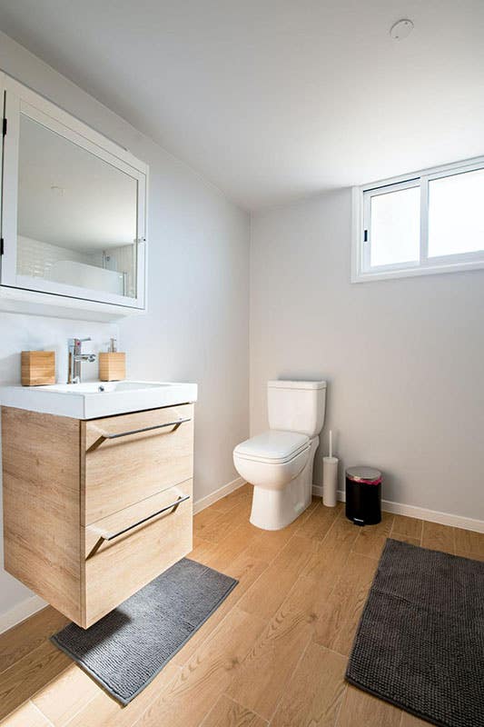 Small bathroom with floating bathroom vanity, mirror cabinet above sink, spc flooring and black floor mat 