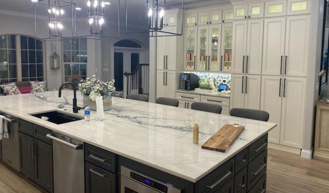 Open kitchen design with white cabinets paired with gray functional island, Pendent lights, Wooden flooring 