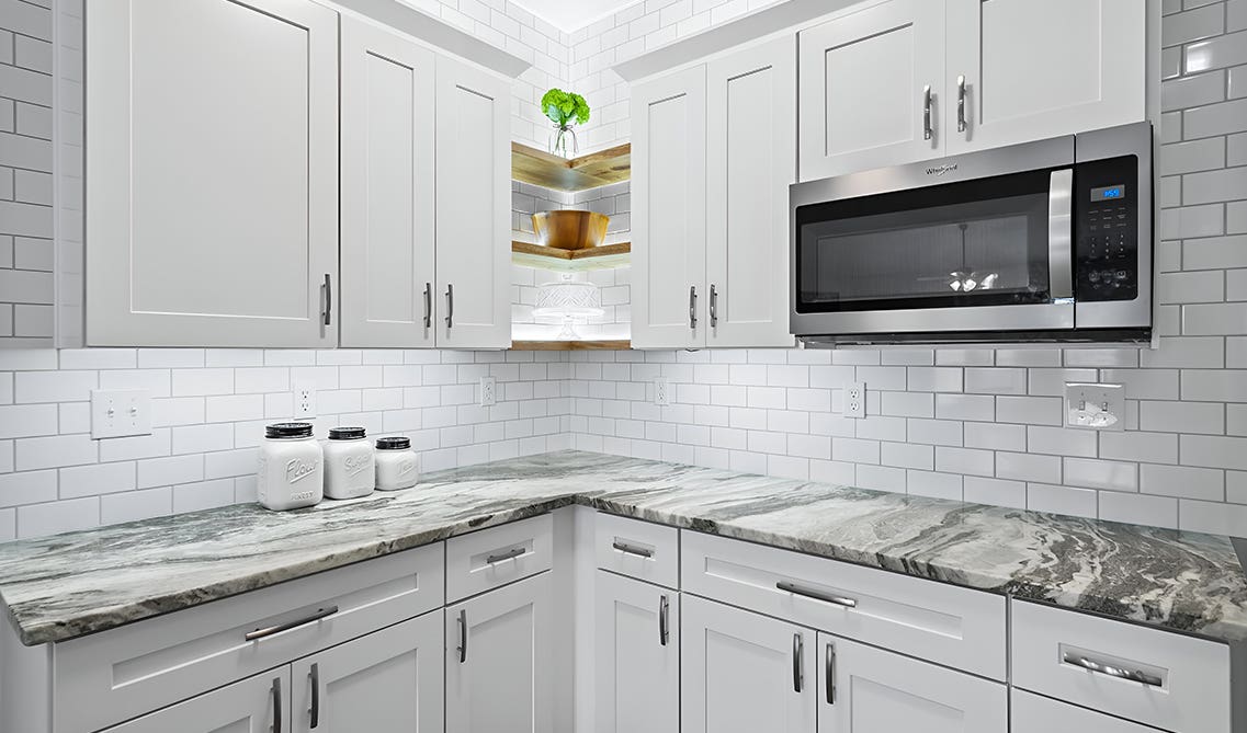 L shape kitchen paired with white shaker cabinets, marble countertop and white subway tiles backsplash
