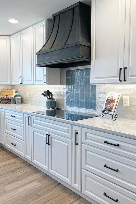 white kitchen cabinets with black hardware, white countertop, black wood hood