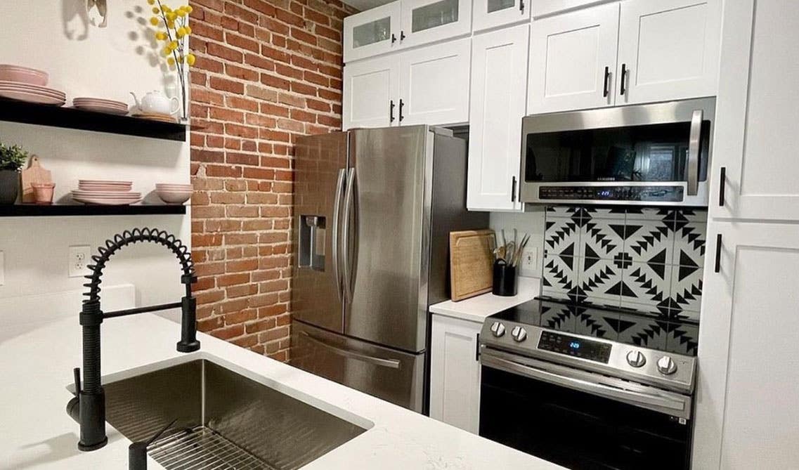 Galley Kitchen Design with white cabinets, island with sink, floating shelves, and rustic brick accent wall 