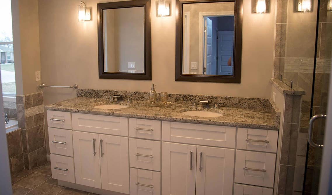 Modern bathroom feature white bathroom vanity with granite countertops, double sink with mirrors and beautiful lamp lights