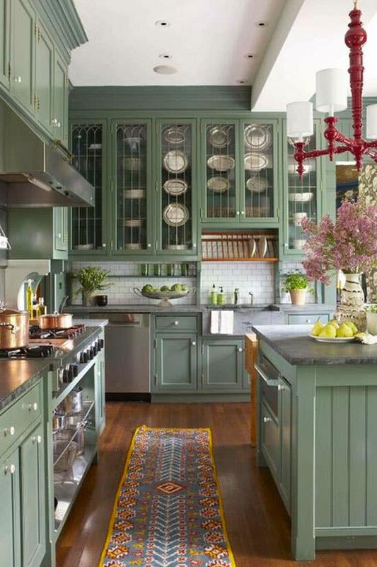 Farmhouse kitchen features green cabinets, concrete waterfall countertops, and wooden flooring 