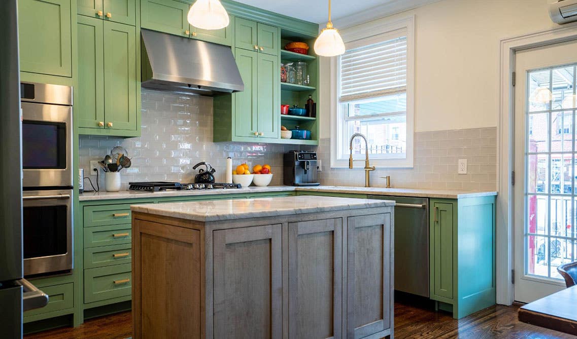 Farmhouse kitchen features Green cabinets With a Grey Island and stainless steel appliances