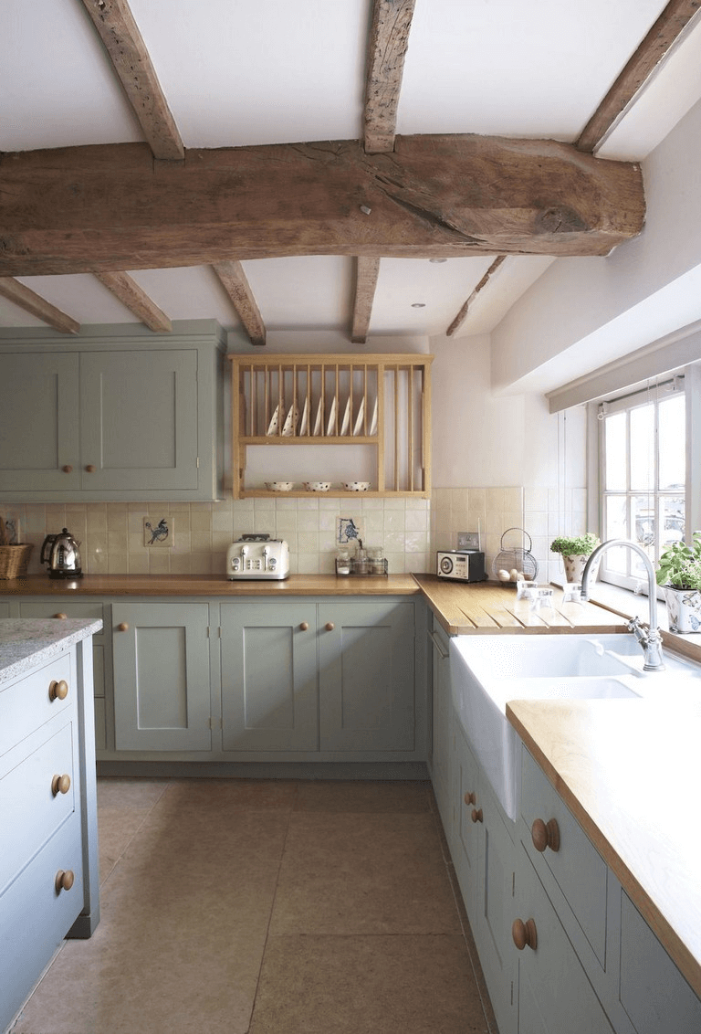 rustic country farmhouse kitchen with light gray cabinetry wood beams and tile floors white walls