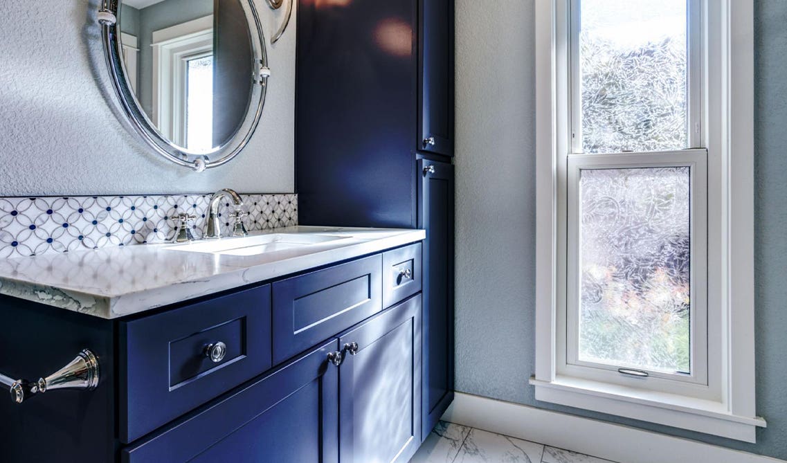 Bathroom design with navy blue vanity, stainless steel fixture and statement mirror 