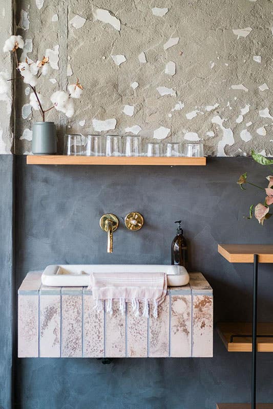 stylish bathroom design with gray and blue accent wall, floating sink and shelves, gold fixture 