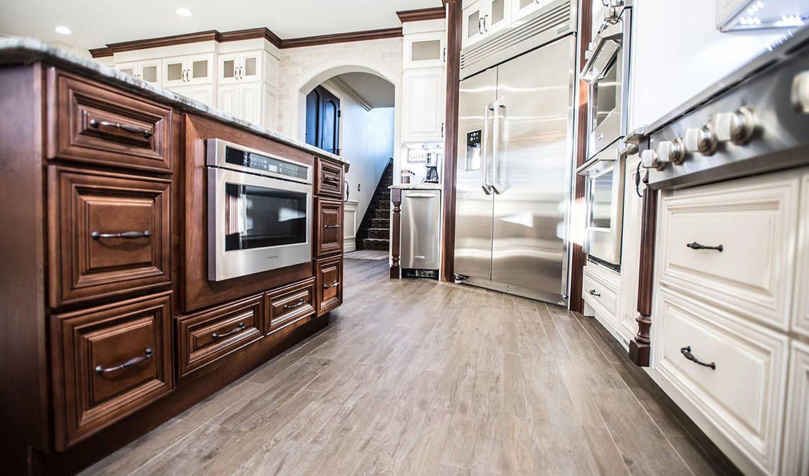 Two tone cream and dark kitchen cabinets with black hardware, stainless steel appliances and spc flooring 