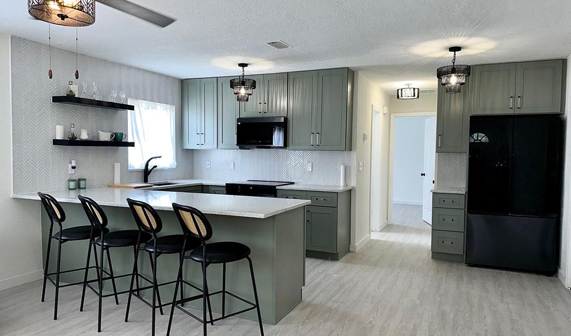 Sage green kitchen cabinets paired with black appliances and white countertop